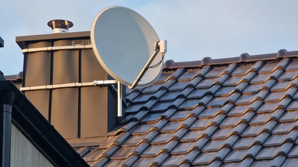 Jasna antena satelitarna zamontowana na kominie. W tle bezchmurne niebo.