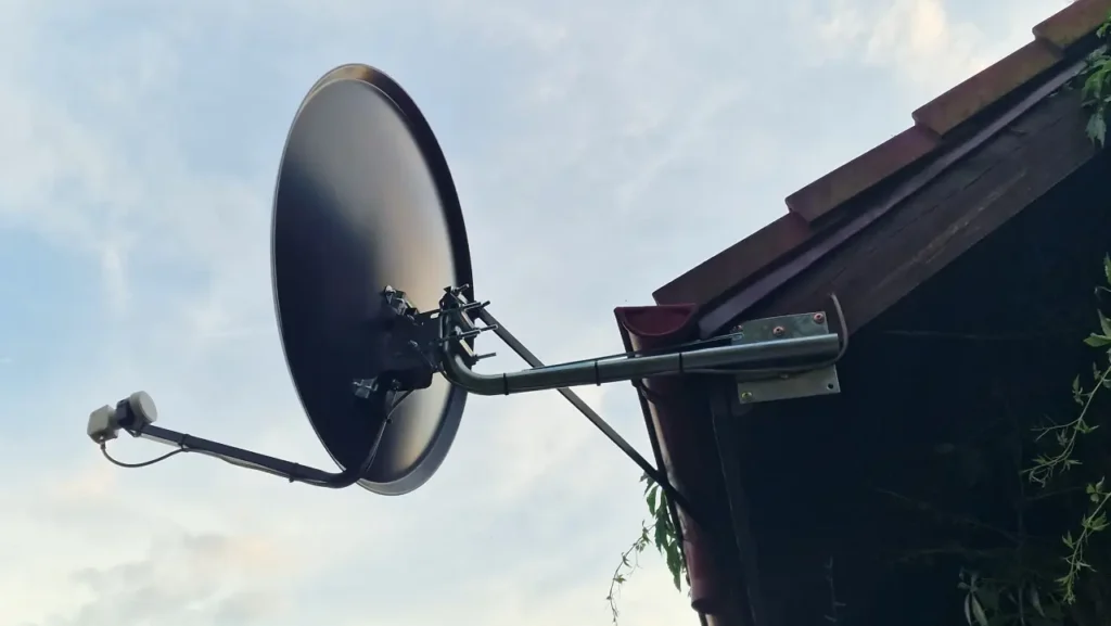 Czarna antena satelitarna pod czarnym dachem. W tle błękitne niebo-białe niebo.