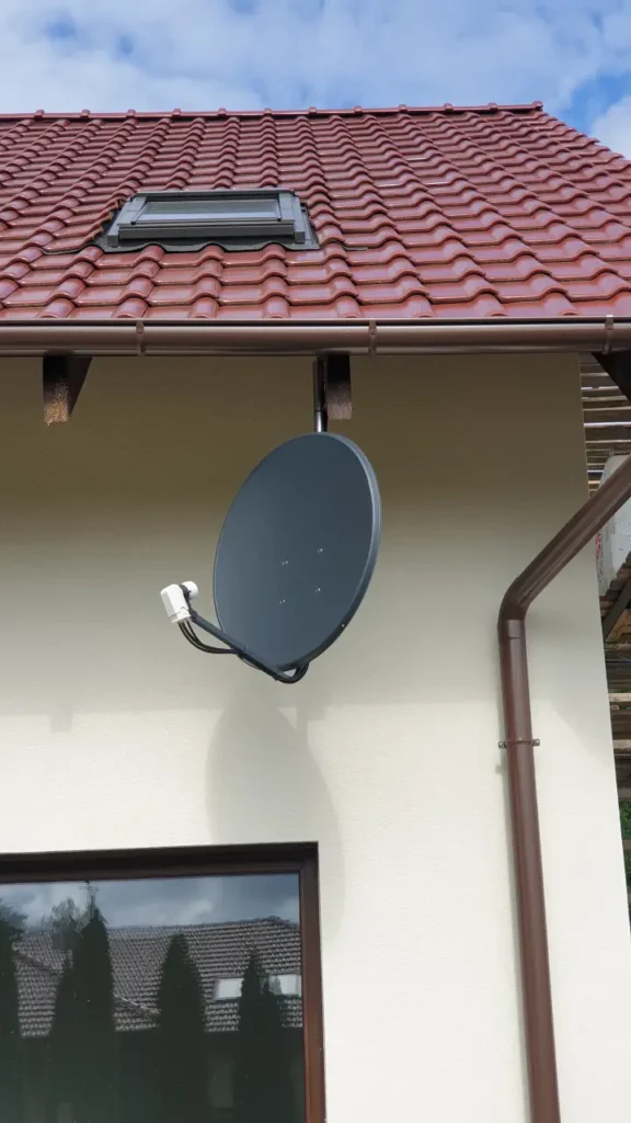Czarna antena satelitarna zamontowana pod dachem. W tle błękitno-białe niebo