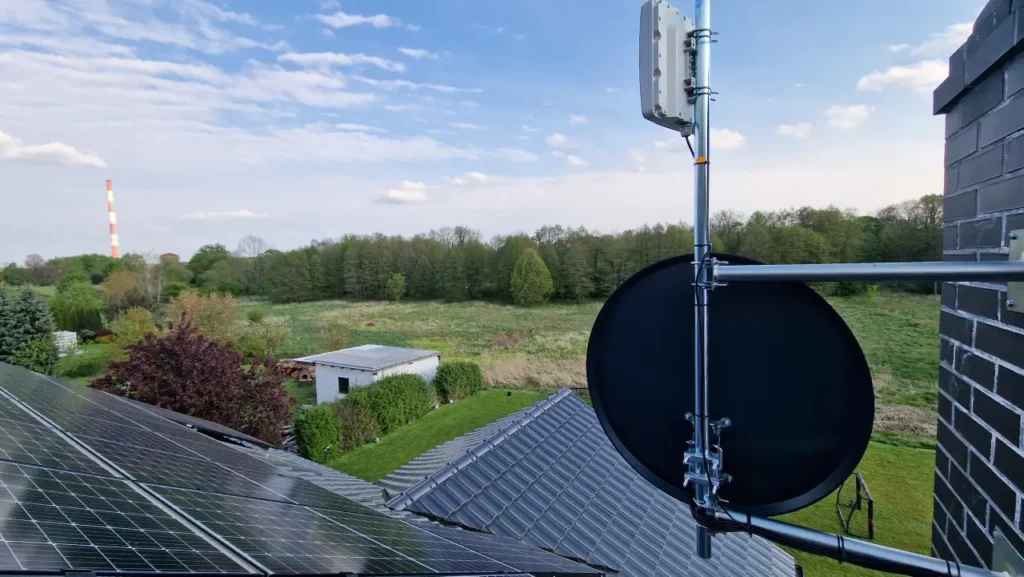 Czarna antena satelitarna na kominie. W tle widok na zielony las