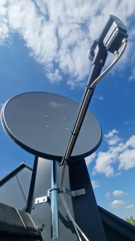 Czarna antena satelitarna na dachu. W tle chmury na błękitnym niebie