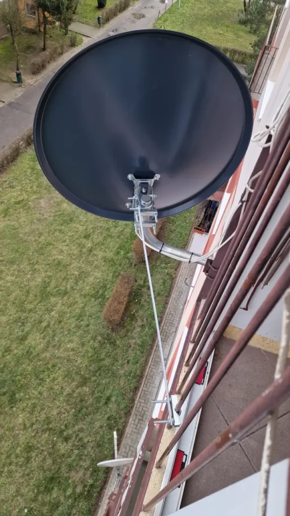 Czarna antena satelitarna na balkonie wysokiej kondygnacji. Widok na trawnik