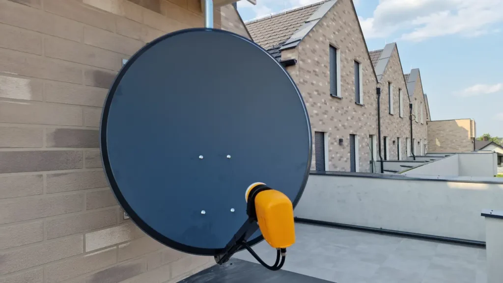 Antena satelitarna z żółtym konwerterem na elewacji szeregowców z różnobarwnej cegły 