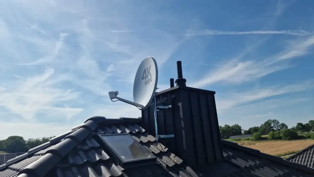 Antena satelitarna 4K Canal+ na kominie na tle błękitnego nieba z jasnymi smużkami