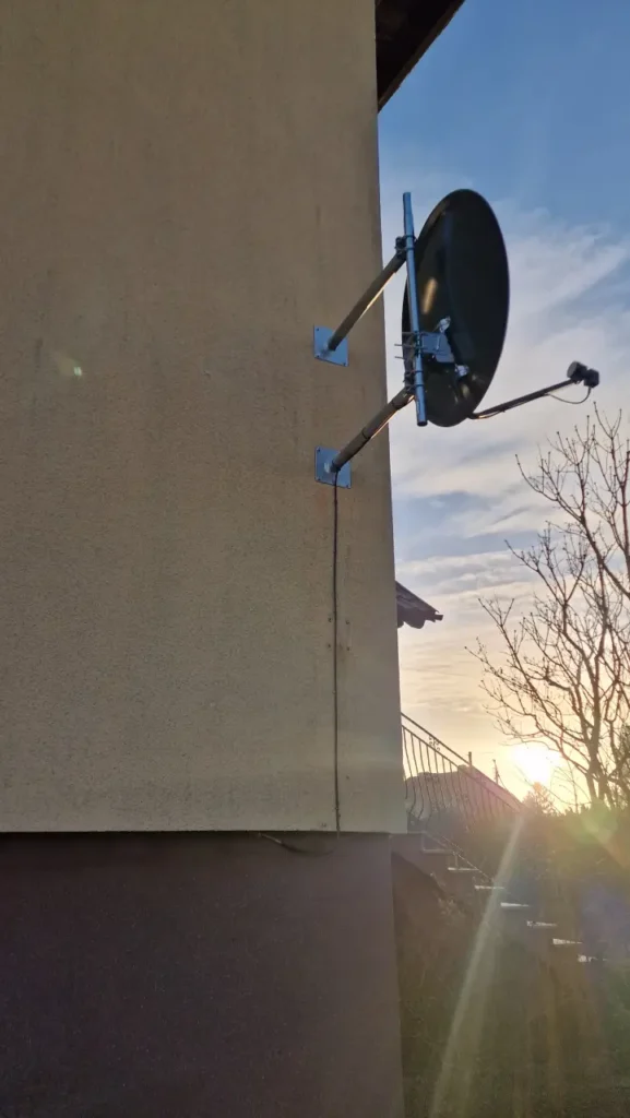 Czarna antena satelitarna na elewacji. w tle zachodzące słońce.