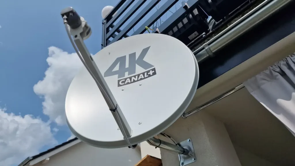 Antena satelitarna 4K Canal+ na elewacji na tle błękitnego nieba z jasnymi chmurami
